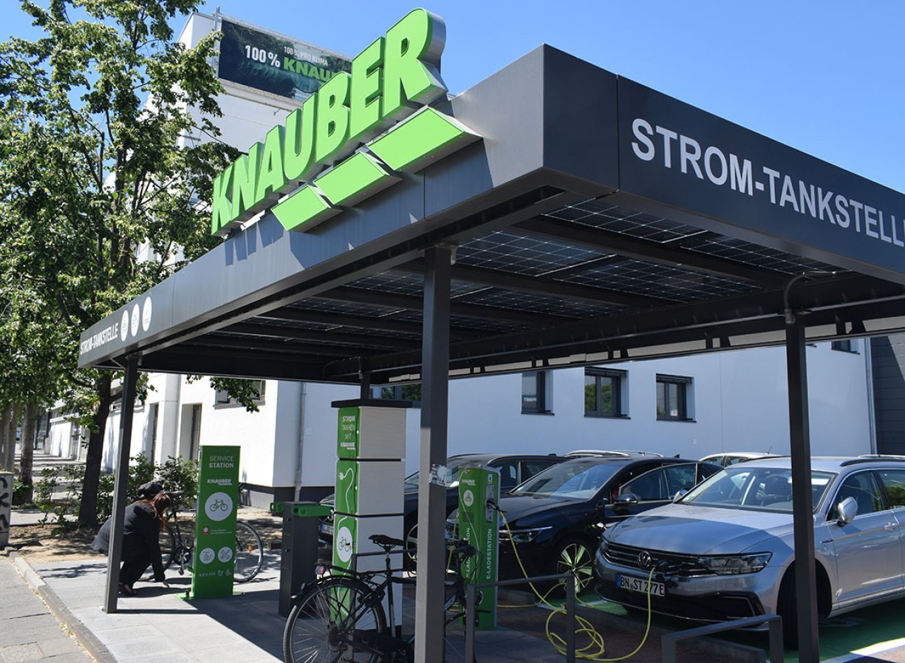 Eine schwarze Stromtankstelle mit der Aufschrift Knauber. Einige grüne Ladesäulen sind unter dem Dach zu sehen.