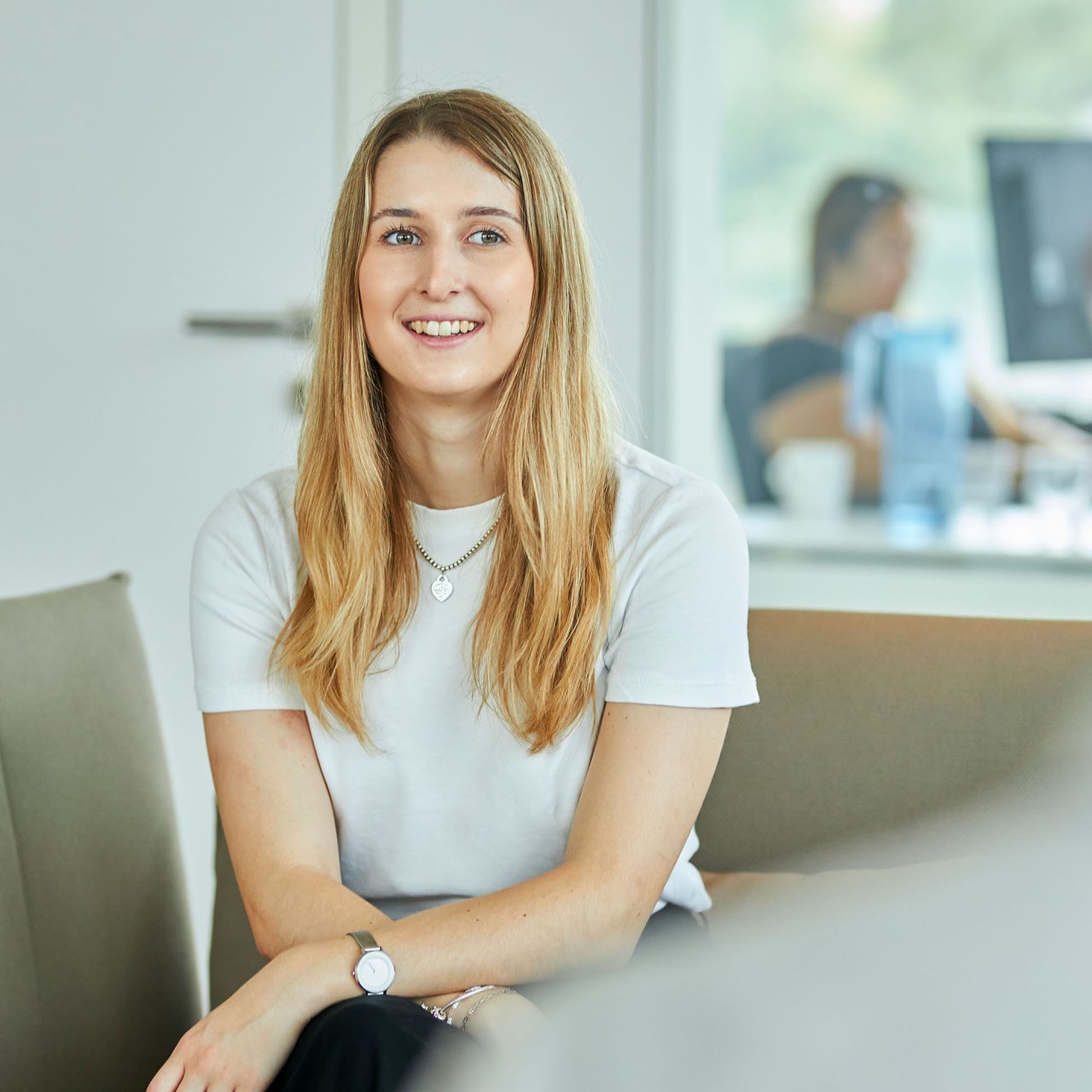 Eine junge Frau mit langen blonden Haaren und weißem T-Shirt sitzt an einem Bürotisch.