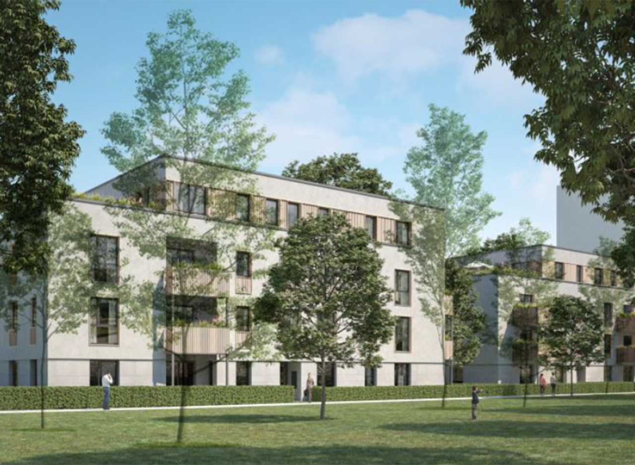 Mehrstöckiges weißes Wohngebäude auf einer grünen Wiese. Vor dem Haus stehen Bäume.