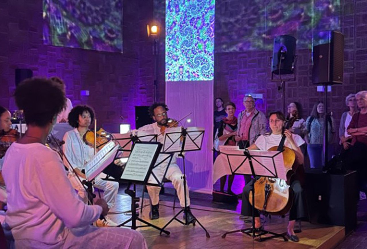 Kammermusikensemble mit Streichinstrumenten spielt vor Publikum in einem Raum mit bunter Lichtprojektion an den Wänden.