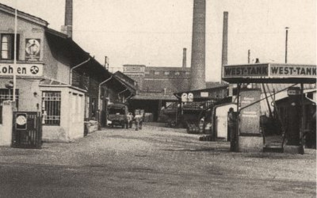 Ein altes Foto einer Straße mit historischen Gebäuden und Autos aus vergangener Zeit.