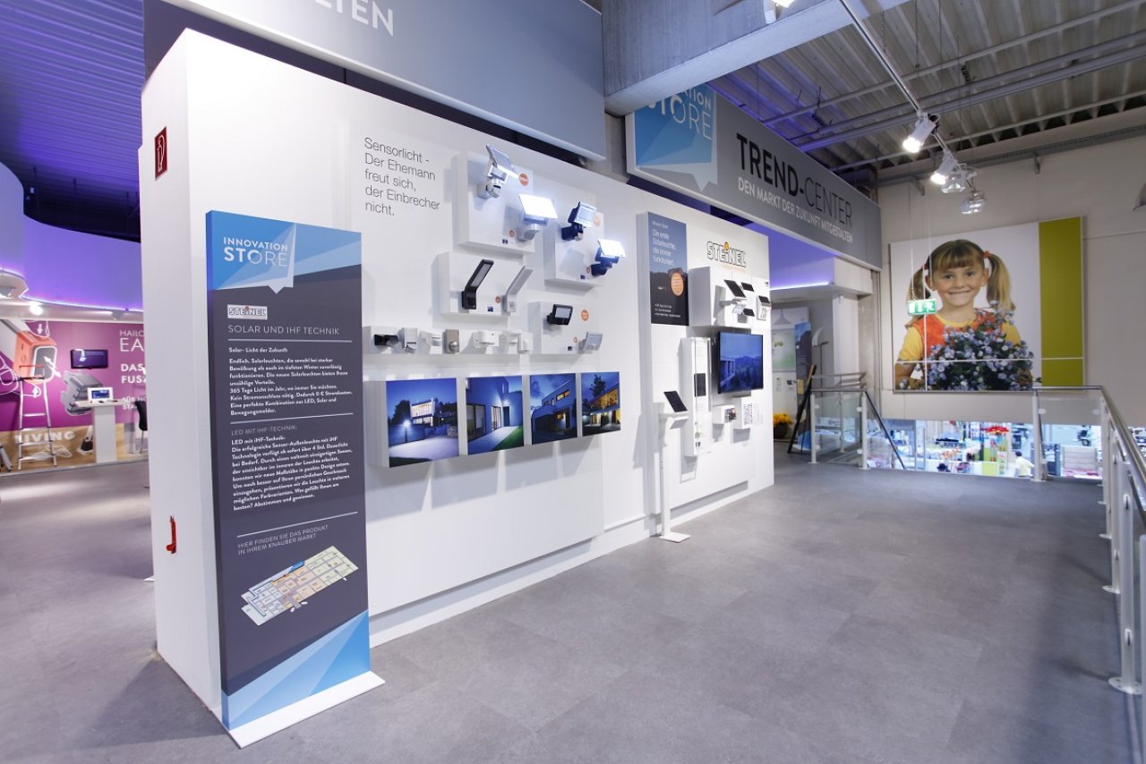 Ausstellung mit weißen Wänden zeigt verschiedene technische Geräte und Informationsbilder zu Solar- und Energiespeicherlösungen in einem modernen Ausstellungsraum.