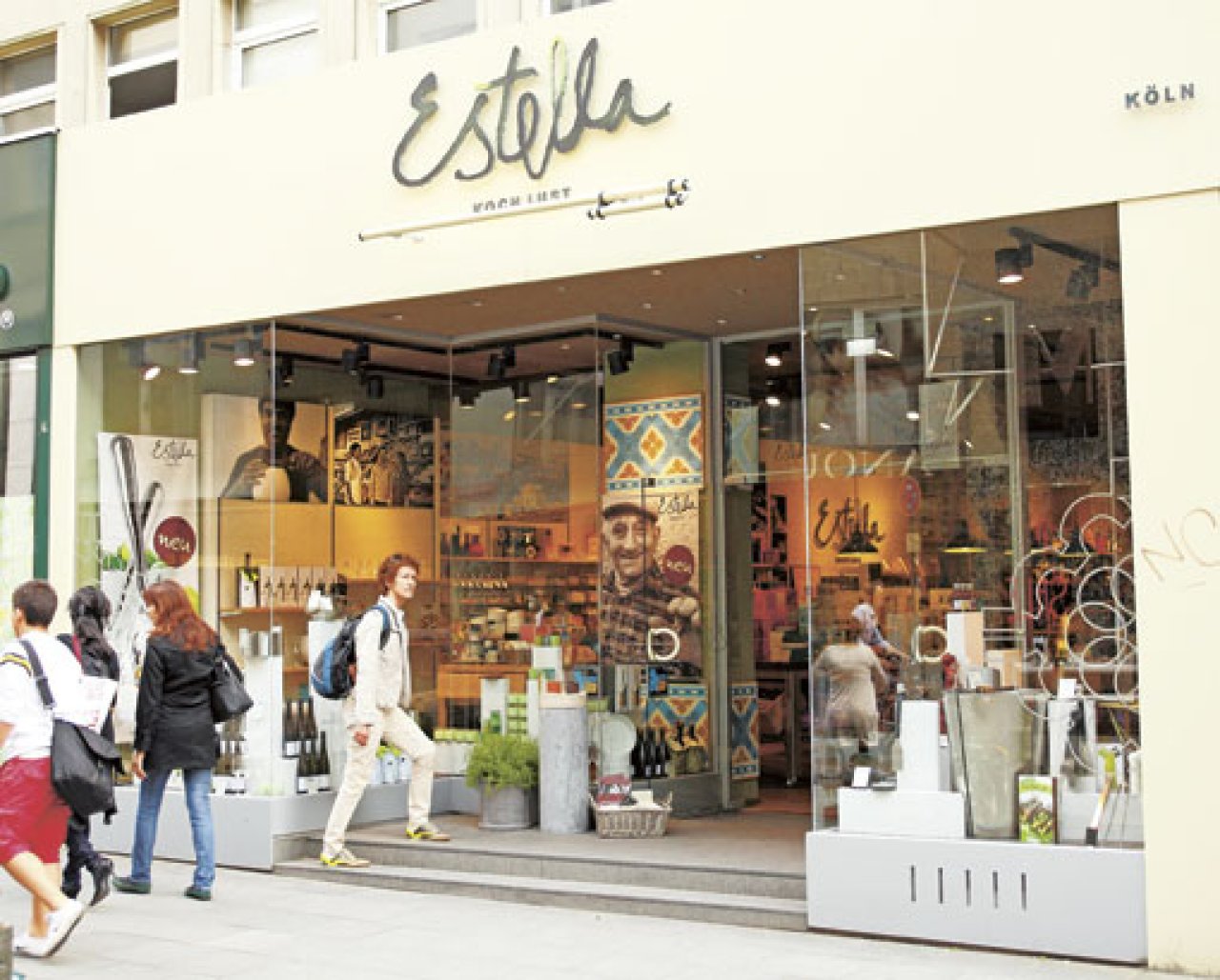 Eingang des Estella Concept Store in Köln mit Glasfront und Menschen, die vorbeigehen.