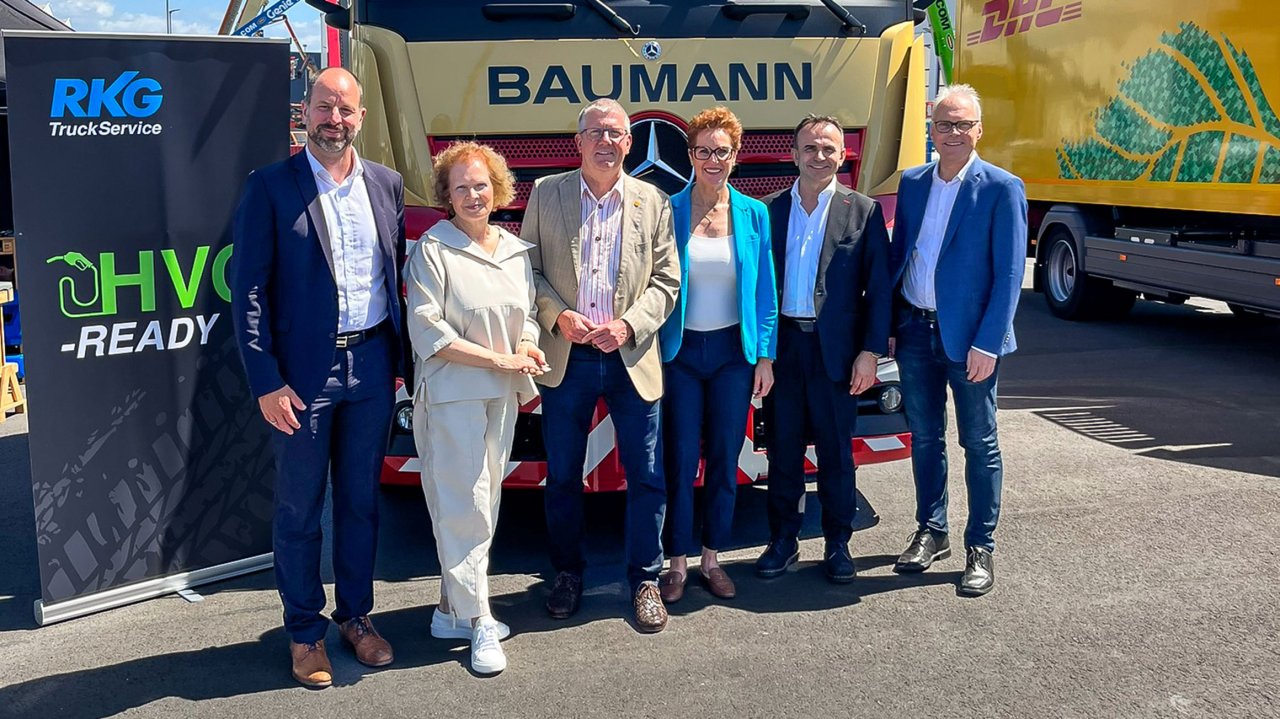 Sechs Personen stehen vor einem gelben Baumann-Lkw, daneben ein Banner mit RKG TruckService und HVO-Ready Schriftzug.