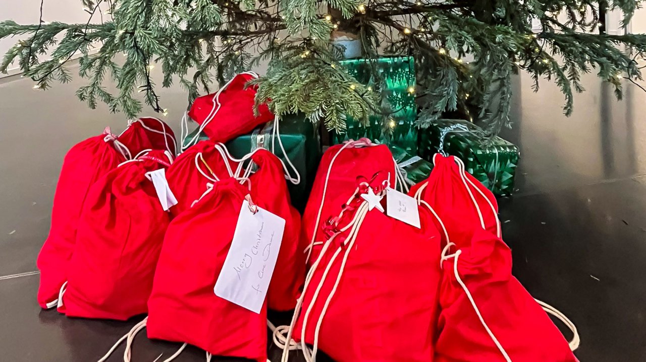 Unter einem Tannenbaum sind mehrere rote Geschenksäckchen zu sehen.