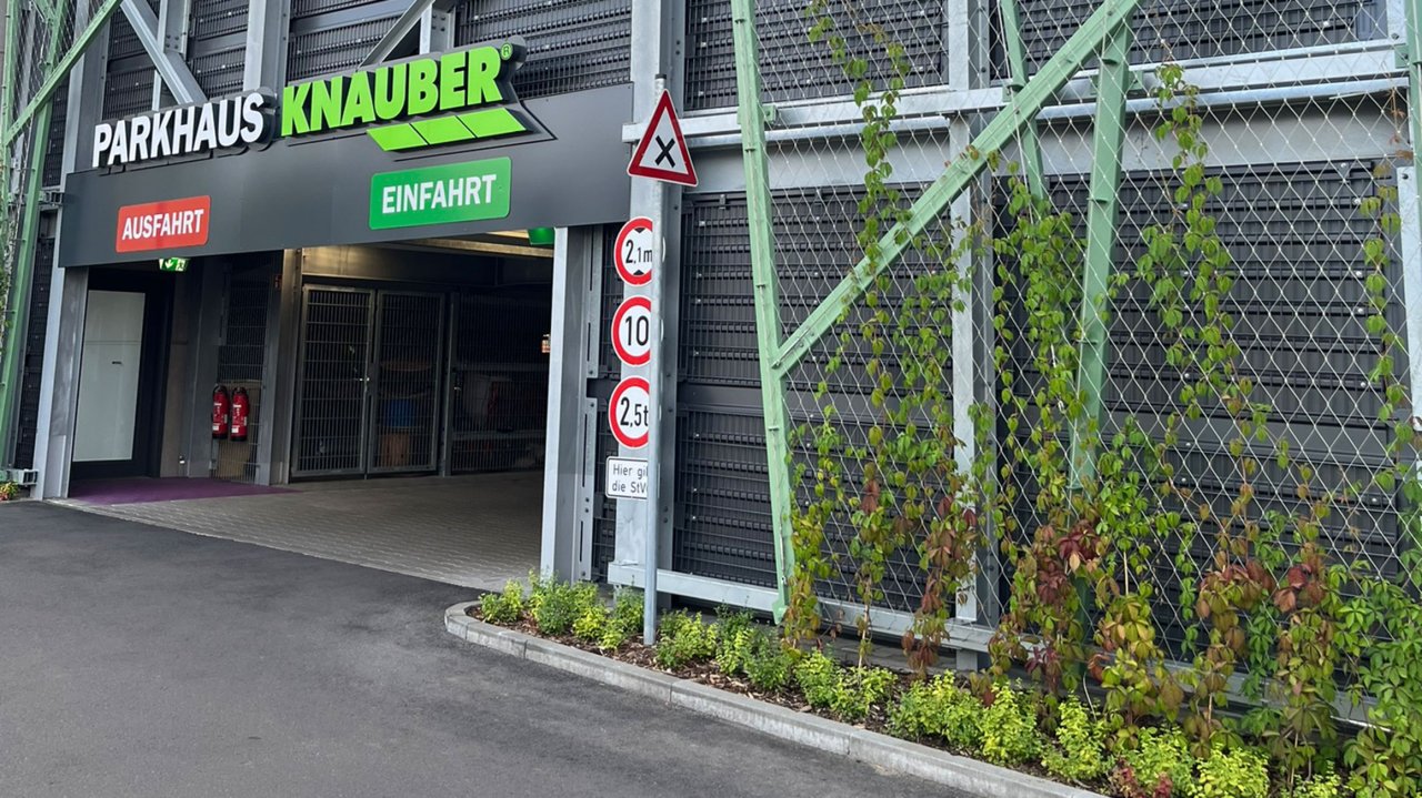 Einfahrt und Ausfahrt des Parkhauses Knauber mit grüner und roter Beschilderung und Verkehrsschildern für Höhen- und Gewichtsbeschränkungen.