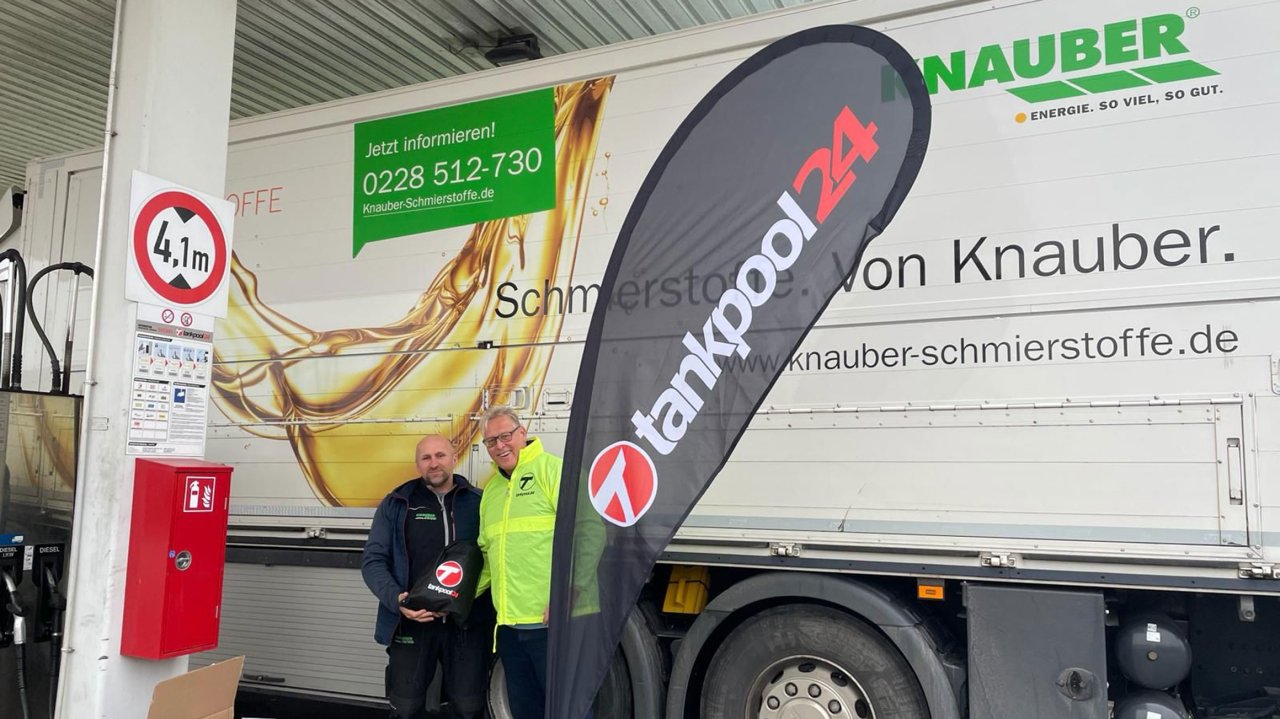 Zwei Männer stehen vor einem Lkw mit der Aufschrift „Knauber Schmierstoffe“ an einer Tankstelle; daneben ein „tankpool24“-Banner und Werbeschilder.