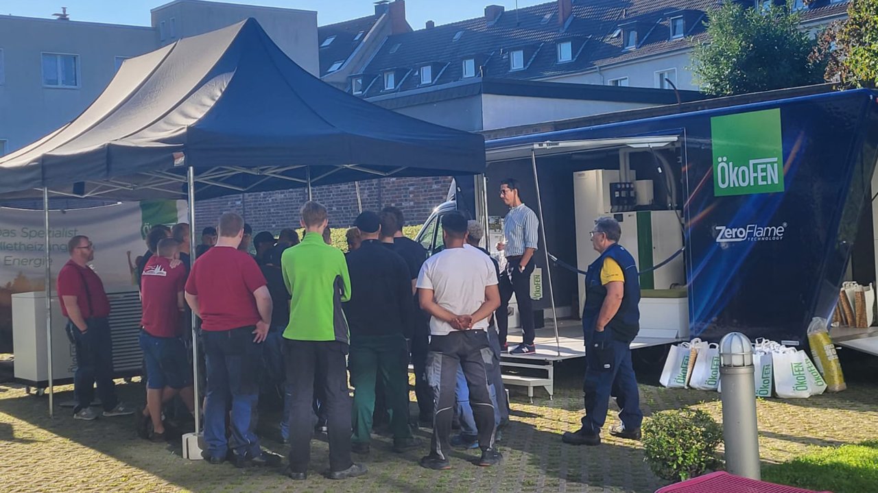 Gruppe von Menschen bei einer Vorführung vor einem Zelt mit ÖkoFEN-Logo und ZeroFlame-Banner im Freien.
